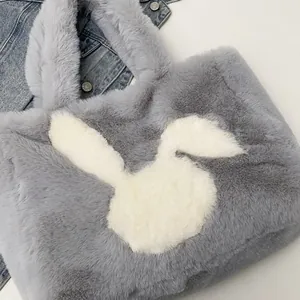 Close-up of soft grey plush tote bag featuring a white bunny motif on denim jacket