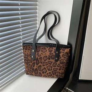 Detail of leopard print tote bag featuring black shoulder straps and gold rivet accents