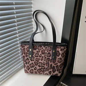 Detail of leopard print tote bag featuring black slim straps and golden rivet accents