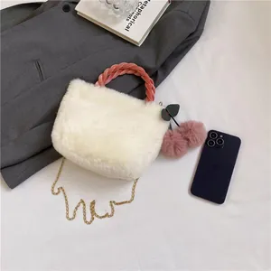 Close-up of white plush bucket bag with pink woven handle and cherry pompom charms