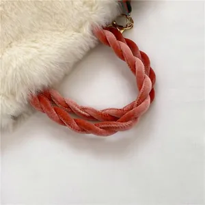 Close-up of plush faux fur handbag with pink velvet knotted handle and gold metal ring