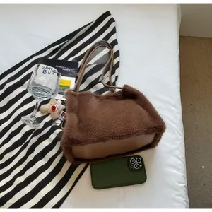 Brown plush tote bag with leather base detail and cute bear charm in cozy setting
