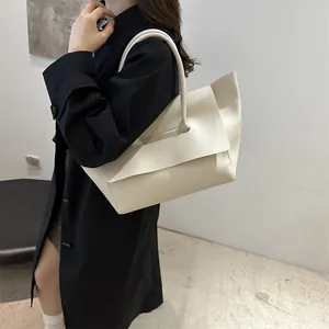 Minimalist beige trapezoid tote bag with large flap shown on a model in a black coat