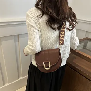 Brown faux leather saddle bag with gold horseshoe buckle and patterned crossbody strap