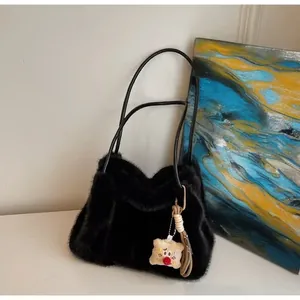 Detail of plush black tote bag with leather straps and a cute beige hanging charm