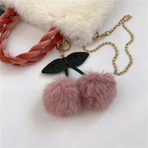 Detail of plush faux fur handbag with pink woven handle and cute cherry charm accessory