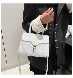 Détail d'un sac à main blanc avec texture crocodile, fermoir rotatif et bandoulière