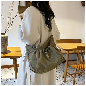 Model wearing a khaki nylon dumpling bag with drawstring closure in a cafe setting