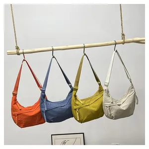 Collection de sacs demi-lune en nylon orange, bleu, jaune et beige suspendus sur bois