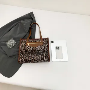 Chic leopard print tote bag with brown leather trim and zipper pocket on white background