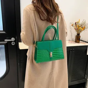 Sac à main vert effet croco avec boucle dorée porté sur un manteau beige élégant