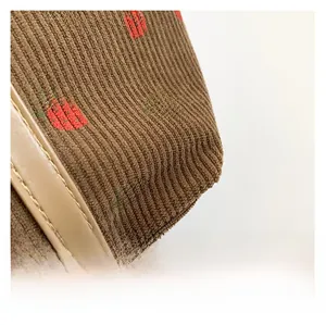 Detail of brown corduroy bag fabric with red strawberry embroidery and leather trim