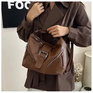 Detail of dark brown PU leather tote bag with metal buckle and zipper accents on brown coat