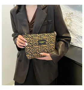 Detail of leopard print makeup bag with gold leather tag held by a fashion model