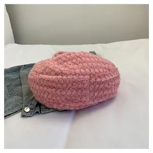 Detail of pink faux shearling heart-shaped bag on white bedding with denim jacket