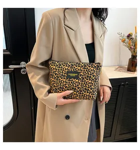 Detail of a leopard print cosmetic bag held by a person in a stylish khaki outfit