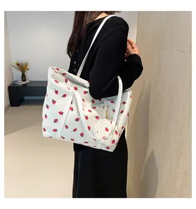 Detail of white corduroy tote bag featuring red strawberry prints and round coin purse