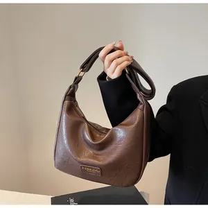 Détail du sac hobo marron montrant la finition en cuir texturé et le logo de marque