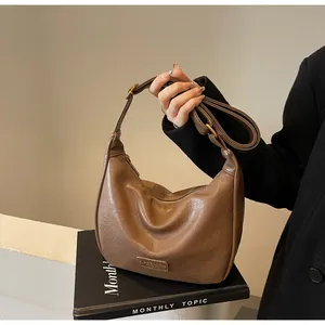 Gros plan du sac demi-lune marron texturé avec bandoulière réglable et détails dorés