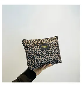 Detail of leopard print makeup bag featuring a black leather logo patch and metal zipper