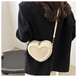 Cream heart-shaped crossbody bag worn over a black blazer, showing fashion strap detail