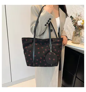Close-up of black corduroy tote bag featuring red strawberry prints and leather straps