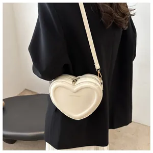 Close-up of a cream heart-shaped crossbody bag with gold hardware and embossed lettering