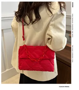 Détail du sac matelassé rouge avec chaîne acrylique porté sur une veste en velours beige