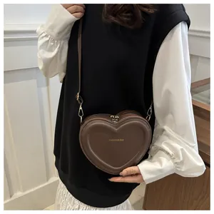 Detail of brown heart-shaped crossbody bag featuring golden fashion text and double zippers