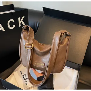 Détail macro du sac bandoulière en cuir marron avec boucle dorée en coffret cadeau