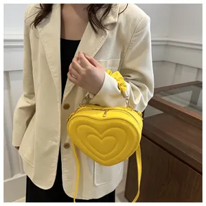 Detailed view of yellow heart-shaped crossbody bag with pleated handle and metal accents