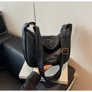 Détail du sac hobo noir avec texture litchi et boucle dorée sur la large bandoulière