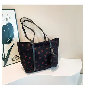Close-up of black corduroy tote bag featuring red strawberry embroidery and matching coin purse