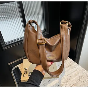 Détail d'un sac à bandoulière en cuir marron vintage avec plis et étiquette logo