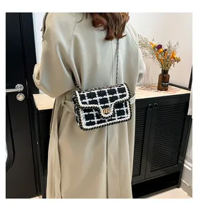 Zwart-witte tweed crossbodytas met gouden kettingriem op de schouder van het model