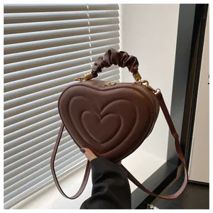 Détail d'un sac marron foncé en forme de cœur avec poignée plissée et accents dorés