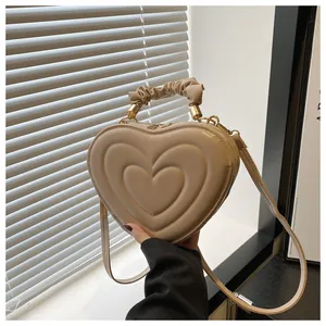 Vue macro du sac cœur beige texturé avec fermoirs dorés et poignée plissée tendance