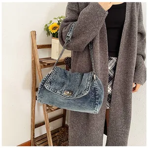 Detailed view of blue denim shoulder bag with metal chain strap and turn-lock closure