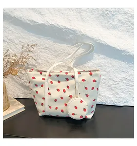 Detail of white corduroy tote bag featuring red strawberry prints and small pouch