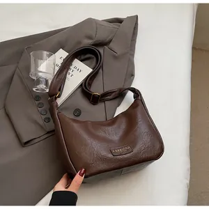 Gros plan du sac à bandoulière en cuir marron foncé à texture plissée et logo en métal