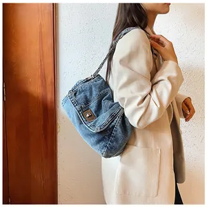 Detail of blue denim shoulder bag with metal turn-lock and chain strap on shoulder
