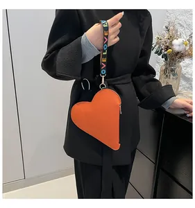 Detail of a stylish orange heart-shaped mini bag with a colorful printed LOVE strap