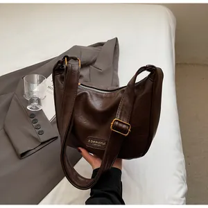 Détail d'un sac dumpling en similicuir marron foncé avec boucles dorées et logo gravé