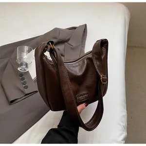 Détail du sac Hobo en cuir plissé marron foncé avec bandoulière réglable sur le lit