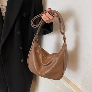 Sac hobo marron en cuir avec large bandoulière porté par un mannequin en blazer noir
