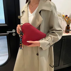 Red heart-shaped leather handbag with a wide LOVE woven strap shown in a lifestyle setting