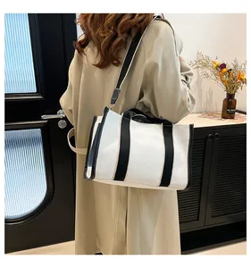 Detail of a large canvas tote bag with contrast black straps and shoulder strap on a model