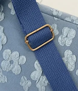 Detail of blue embossed floral pattern bag with gold adjustable buckle on woven strap