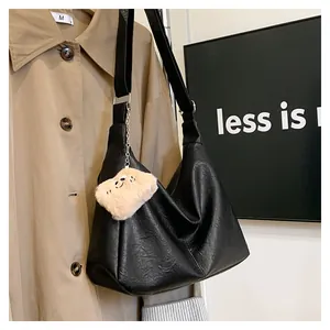 Detail of black pebbled leather hobo bag with a plush charm against a khaki coat