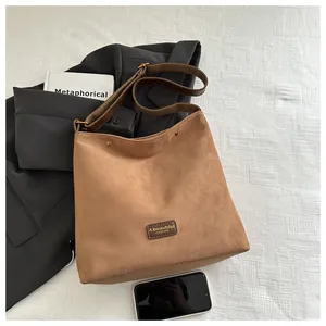 Detail showing brown suede tote bag with leather label and wide fabric shoulder strap